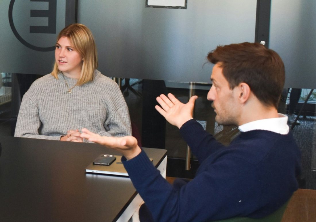 Two people in conversation at a meeting table, one gesturing as he explains a point